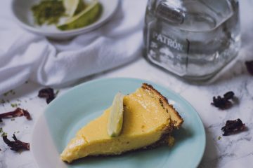 Slice of margarita pie with a bottle of tequila and limes in the background