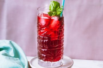 Tall glass with red iced tea and a basil garnish