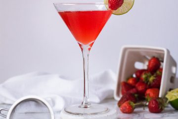 Martini glass with a red drink garnished with a strawberry and lime wheel