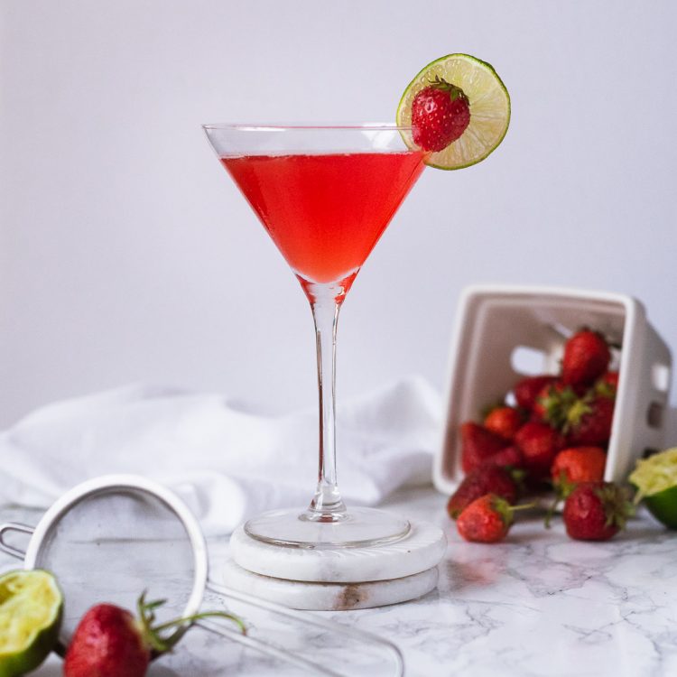 Martini glass with a red drink garnished with a strawberry and lime wheel