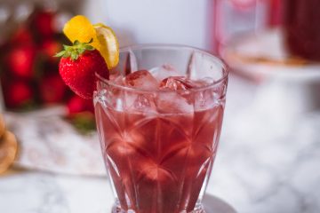 Bramble cocktail in a clear glass filled with ice with strawberries in the background
